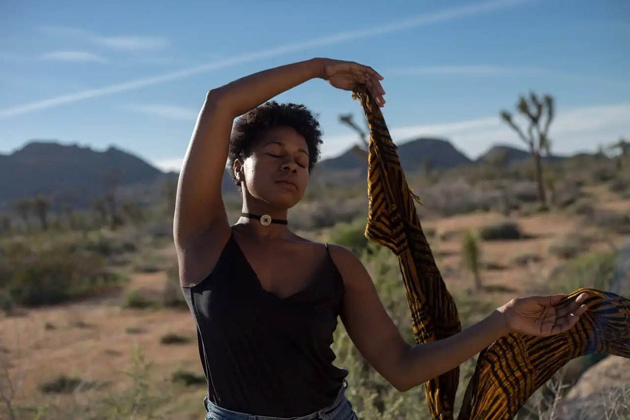 Mulher praticando meditação ao ar livre no deserto, uma dica para melhorar a saúde física e mental, com cenário de montanhas ao fundo.