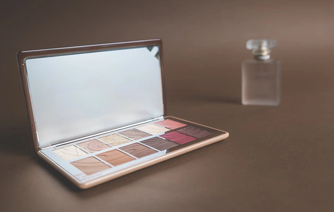 Paleta de maquiagem com cores variadas ao lado de um vidro de perfume, ideal para quem busca dicas de como trabalhar na área da beleza.